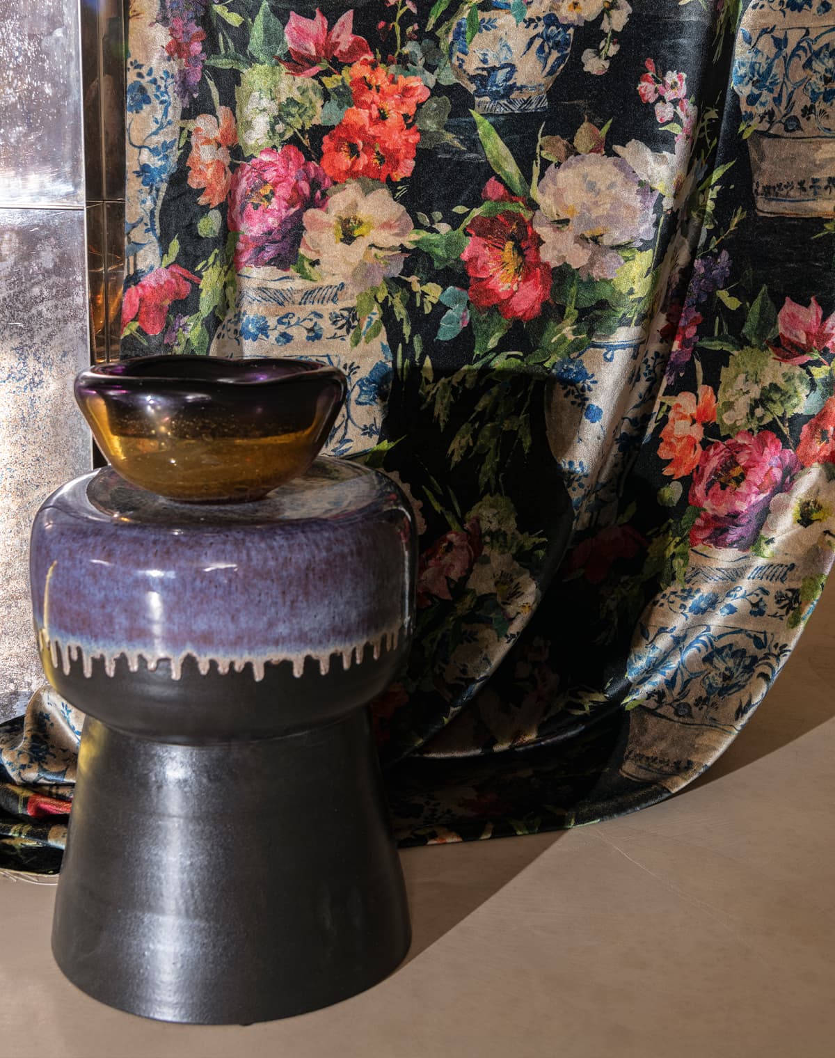 Schwarzer Hocker mit Vase vor einem Vorhang mit floralem Printmuster.