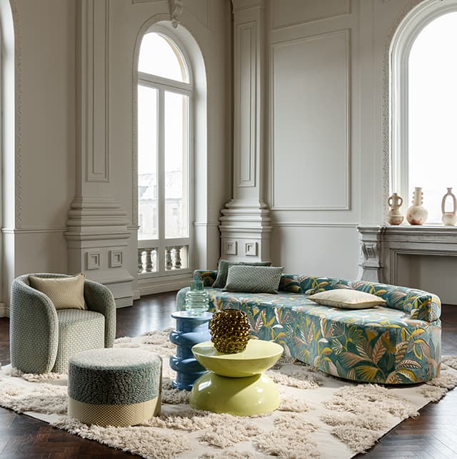 Ein Sofa mit floralem Muster und ein grauer Sessel in einem Saal.