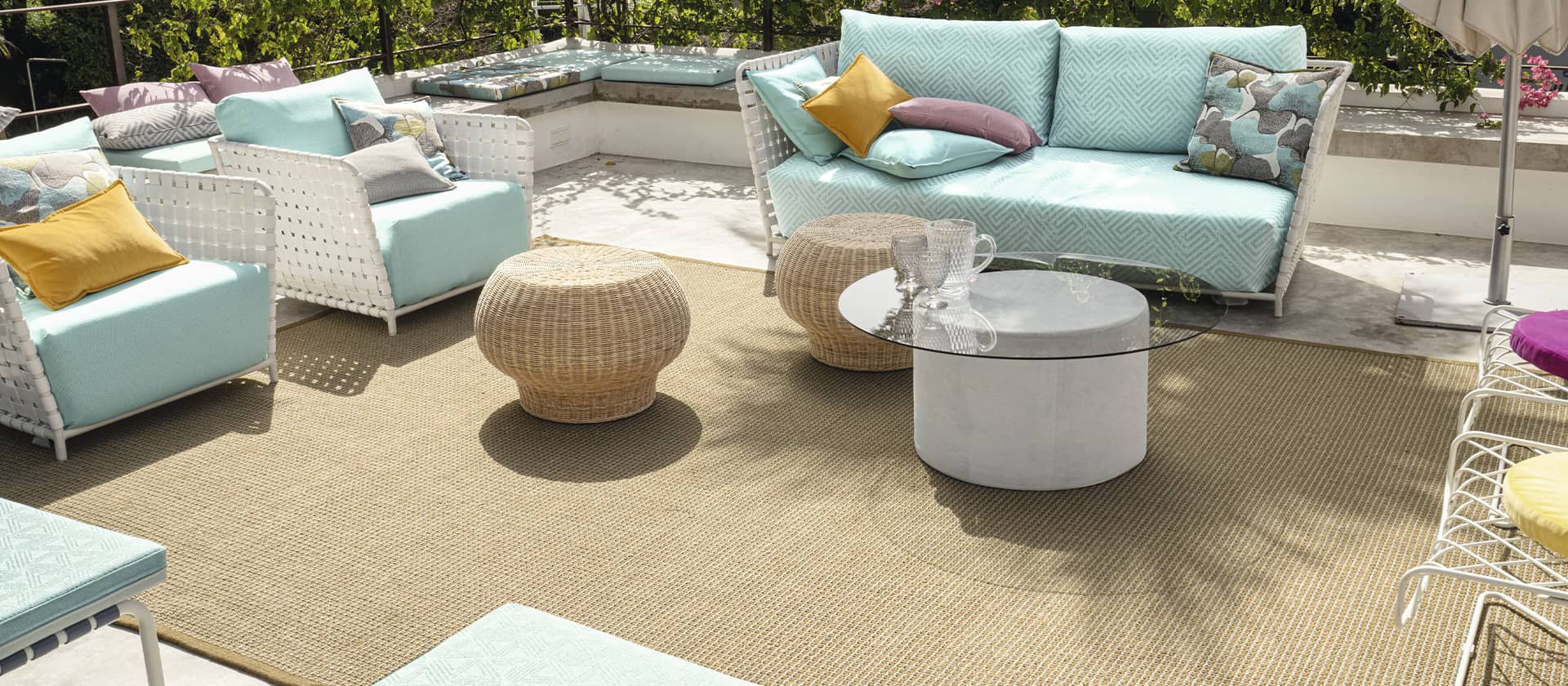 Outdoor-Lounge mit türkisen Sitzmöbeln und einem Teppich in beige auf einer Terasse