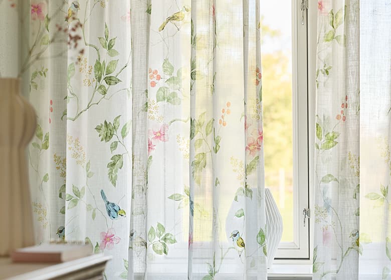 Weiße Gardine mit floralem Print am Fenster.