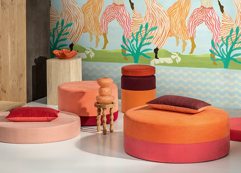 Poufs und Kissen in rosa, rot und orange vor einer Tapet mit Printmotiv