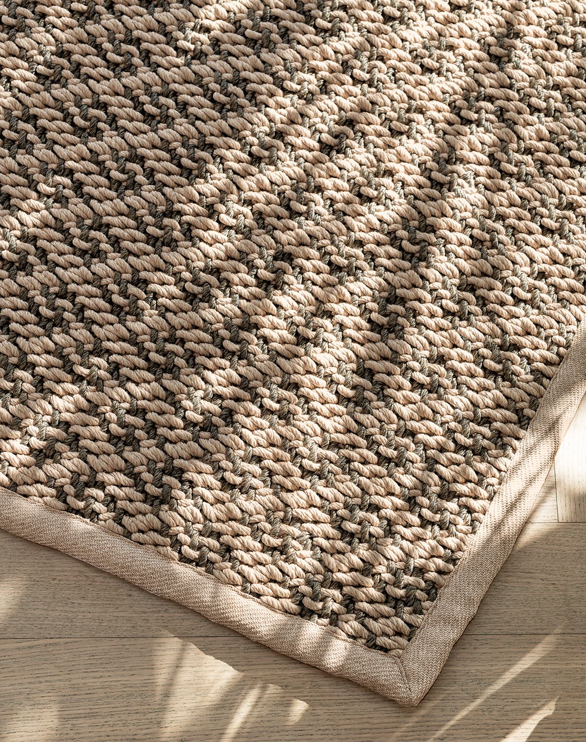 Das Bild zeigt eine Detailaufnahme eines Teppichs in Braun mit leichten dunkelgrünen Akzenten. Die auf den Teppich fallenden Sonnenstrahlen vermitteln ein warmes Gefühl, das durch den Holzboden darunter zusätzlich betont wird.