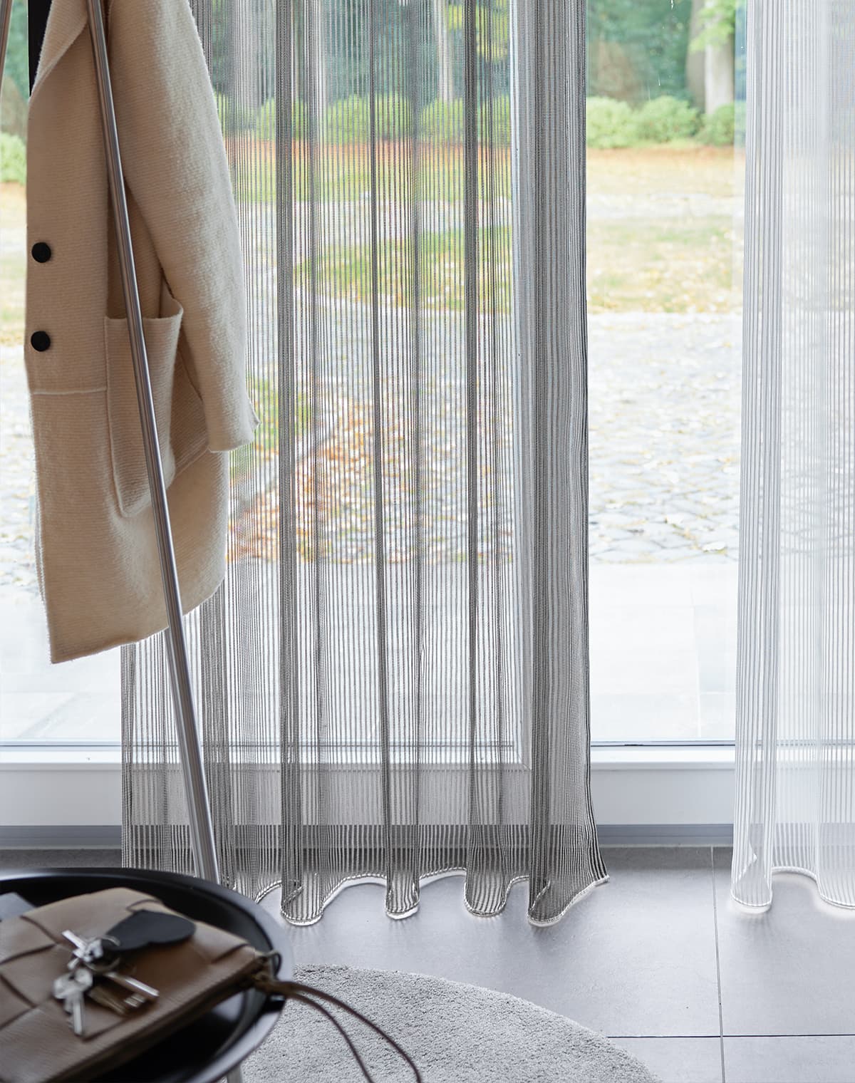 Graue Gardine und Jacke am Jackenständer