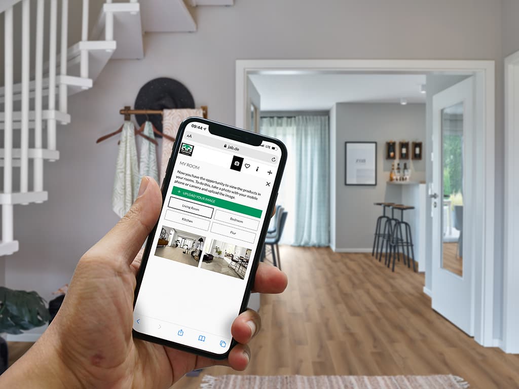 Das Bild zeigt im Eingangsbereich ein Mobiltelefon in der Hand mit dem geöffneten Raumplaner von Adramaq.