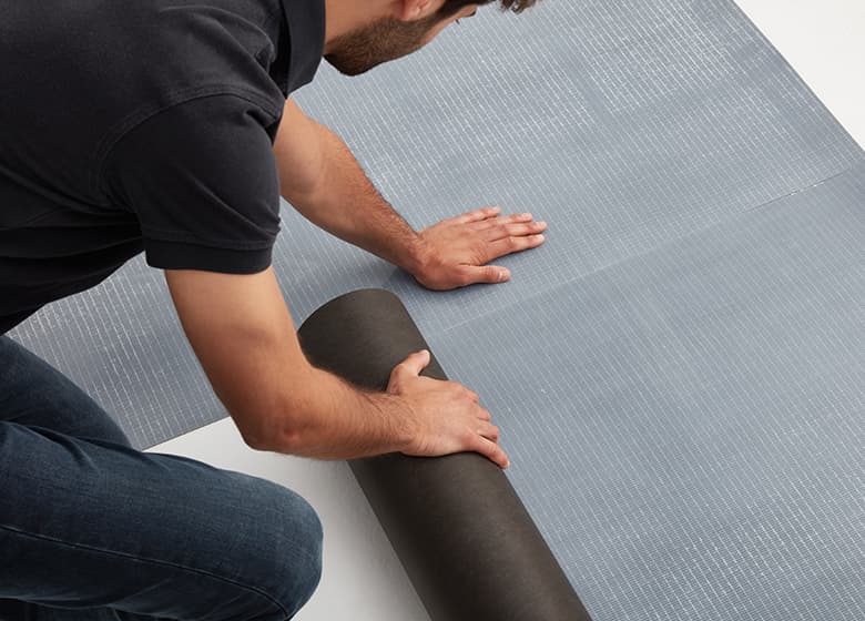 Das Bild zeigt eine Easy Comfort Unterlagsmatte, die gerade verlegt wird. +