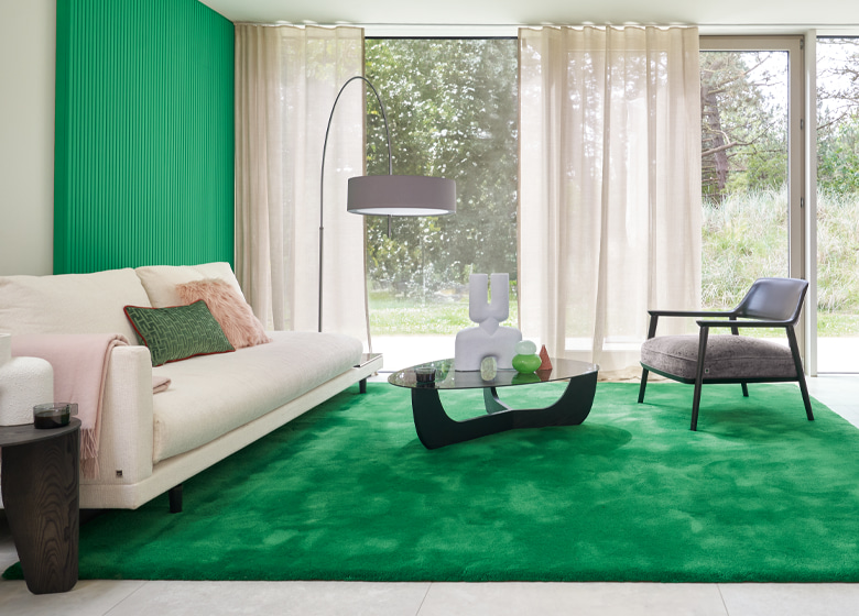 Türkisfarbiger Teppich im modernen Wohnbereich. Hinter dem Sofa steht ein Wandpanel in der selben Farbe wie der Teppich.