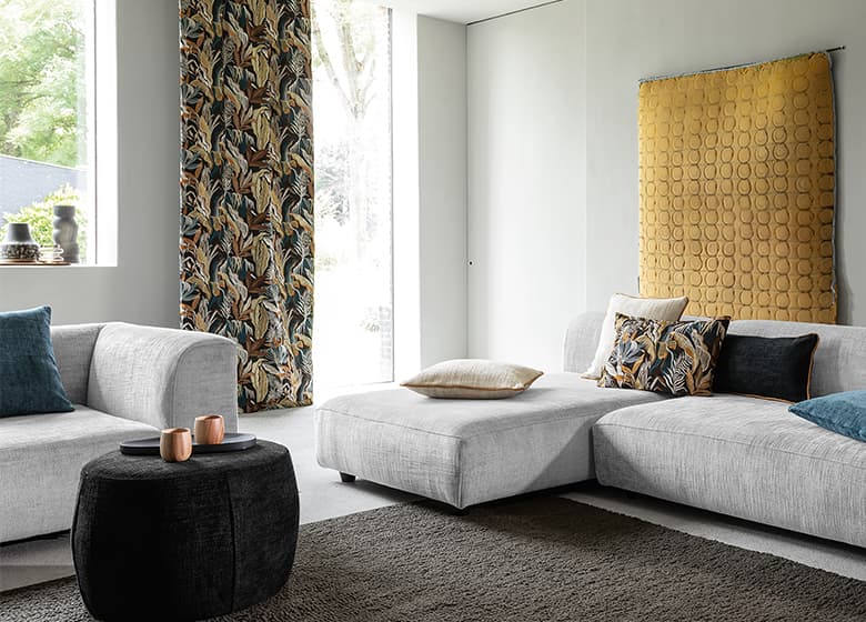 Das Bild zeigt eine weiß-gräuliche Wohnzimmergarnitur in einem Wohnzimmer. Ein dunkler Teppich und ein Wohnzimmertisch sorgen für farbliche Abwechslung. Weitere Accessoires tragen zur gemütlichen Atmosphäre bei.
