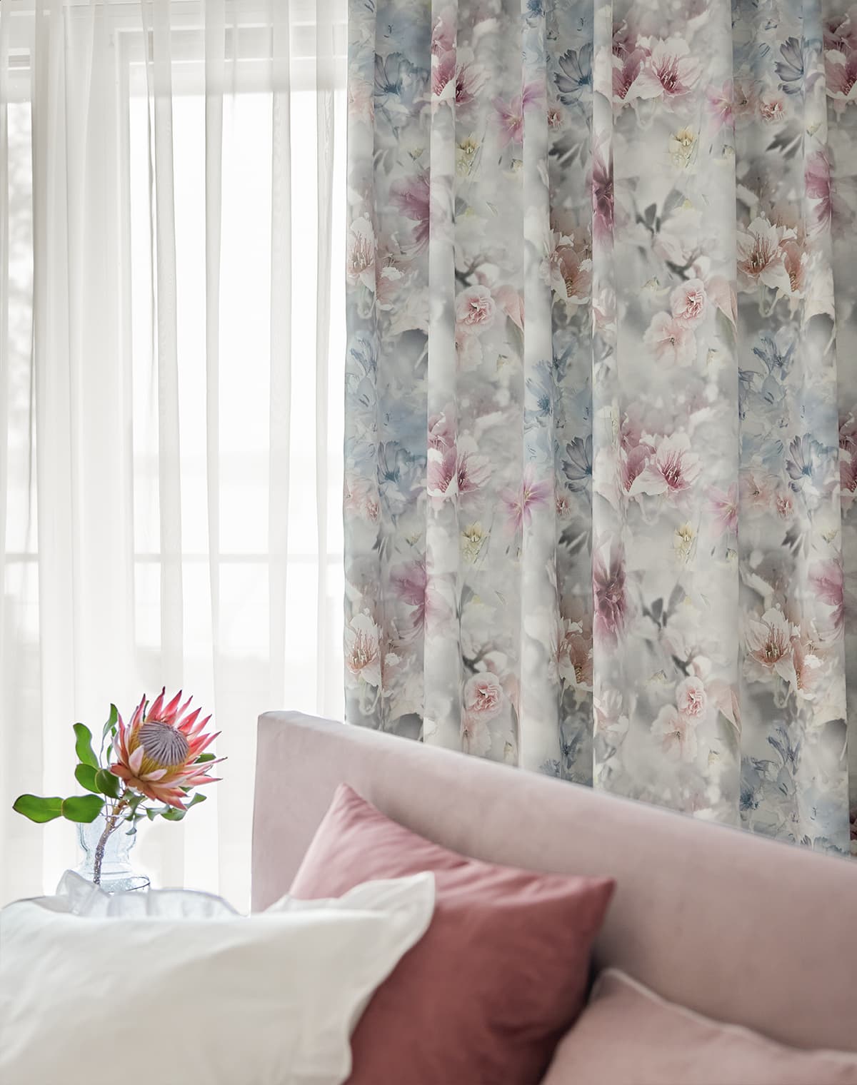 Das Bild zeigt eine Gardine mit floralem Muster im Schlafzimmer. Die Gestaltung des Bettes und die dekorative Zimmerpflanze harmonieren perfekt mit der Gardine und schaffen eine einladende Atmosphäre.