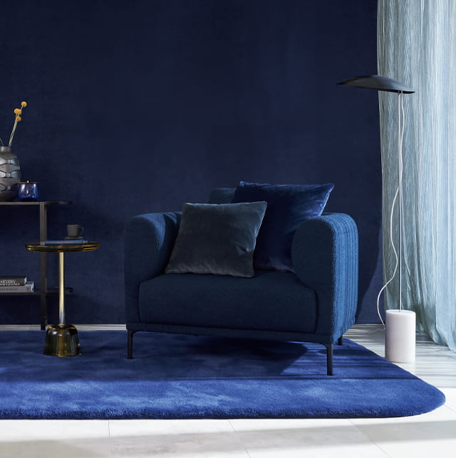 Wohnbereich mit blauer Wand und farbig passenden Möbeln. Auf dem Boden liegt eine blauer Teppich.
