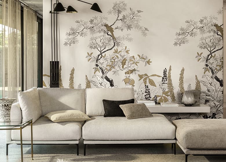 Weißes Sofa mit Kissen in beige, weiß und schwarz vor einer Tapete mit floralem Printmotiv.