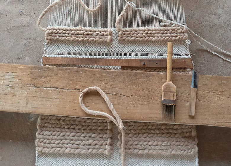 Das Bild zeigt einen weißen Teppich in einem nachgestellten Produktionsschritt, zu dem verschiedene Accessoires gelegt sind.