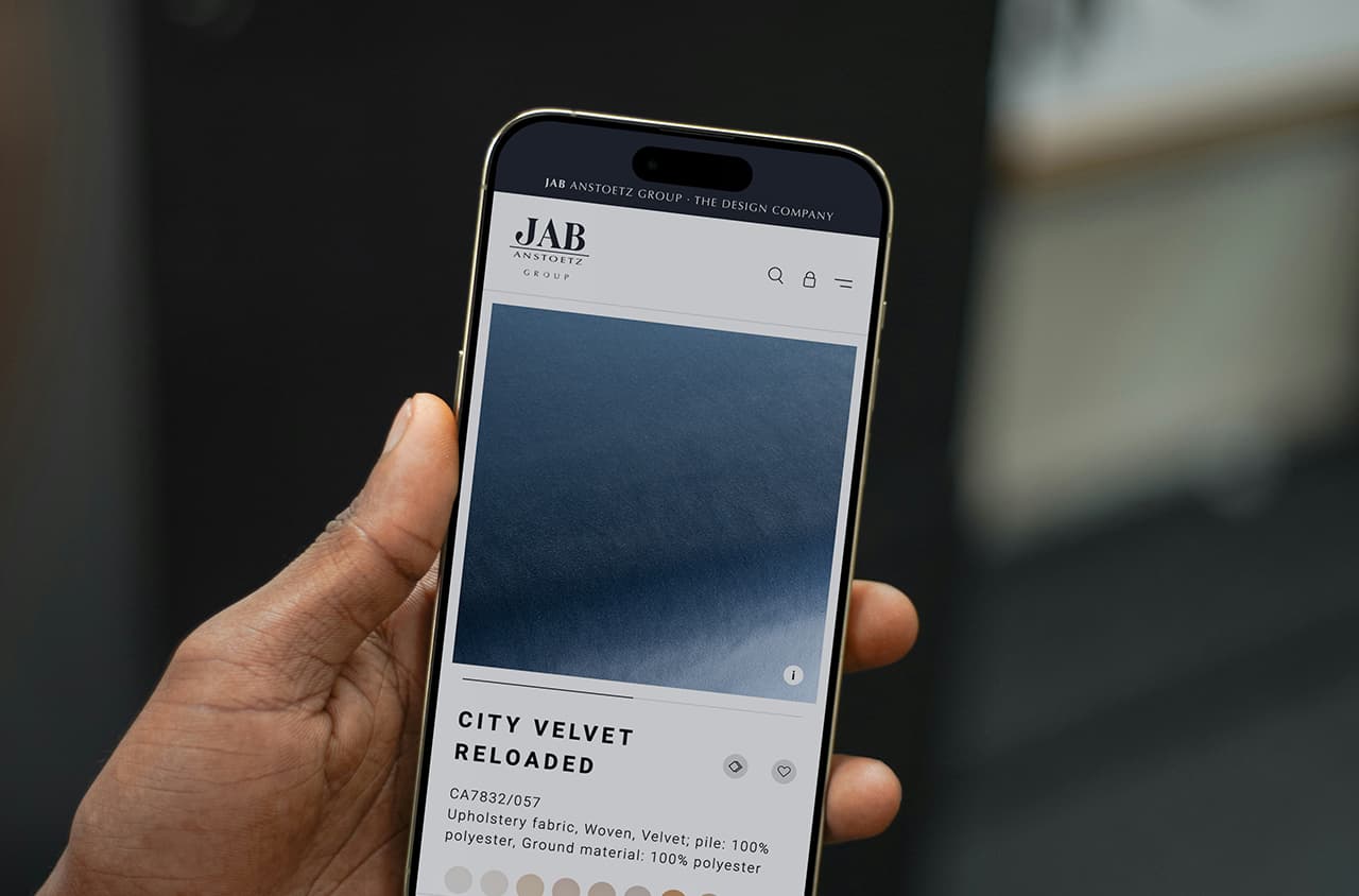 Smartphone with JAB ANSTOETZ Group website showing blue velvet fabric product.