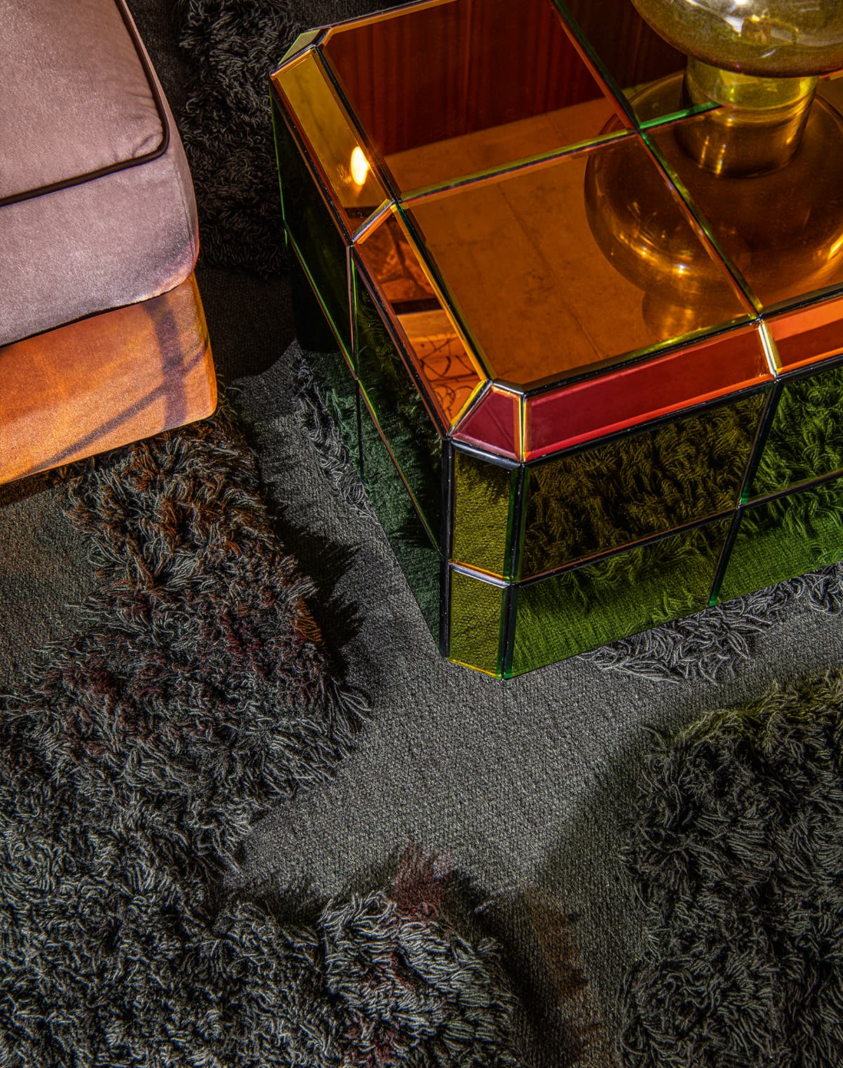 Das Bild zeigt eine Ecke eines Wohnzimmers mit einem braunen Sofa, einem verspiegelten, sechseckigen Beistelltisch und einem schwarzen, flauschigen Teppich.