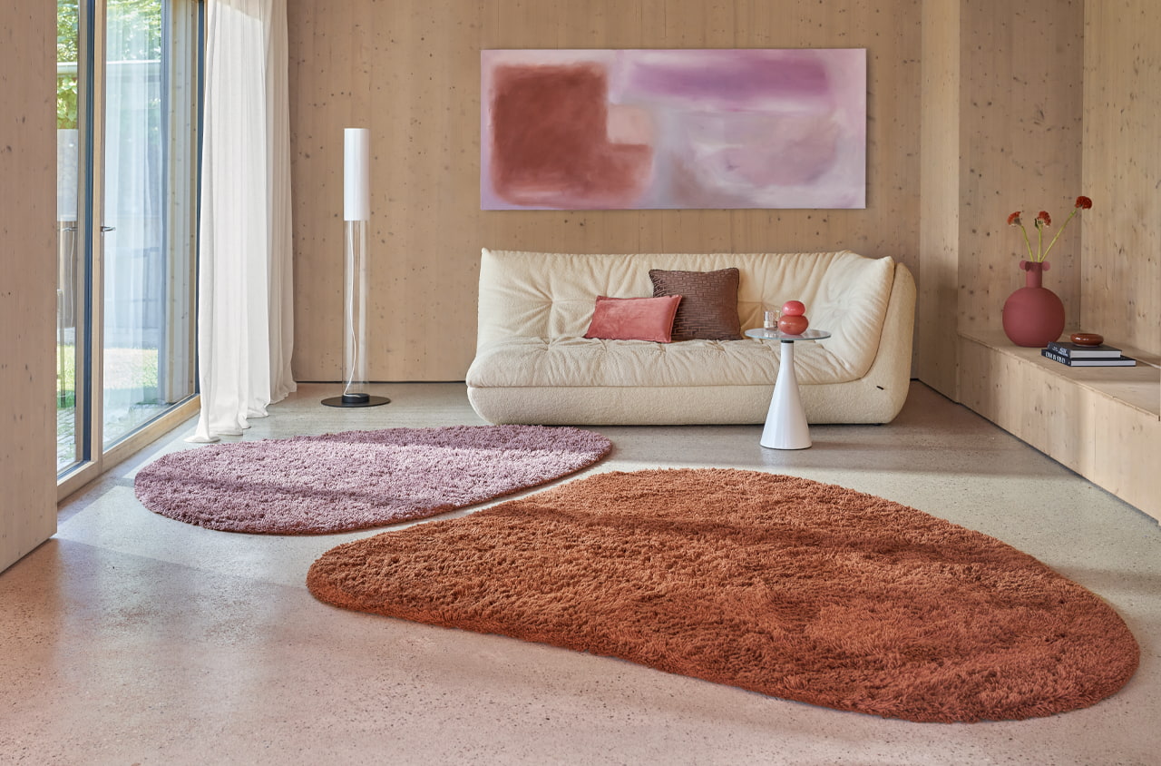 Heller Wohnbereich im Holzvertäfelung. Mittelpunkt ist ein modernes Sofa, und zwei Teppiche in Organischen Formen.