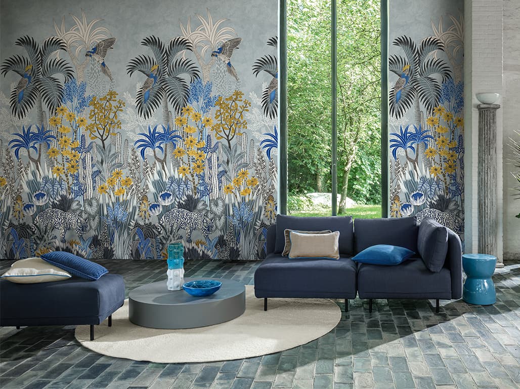 Blaue Sitzlandschaft mit blauen und weißen Kissen vor einer Tapete mit floralem Printmotiv.