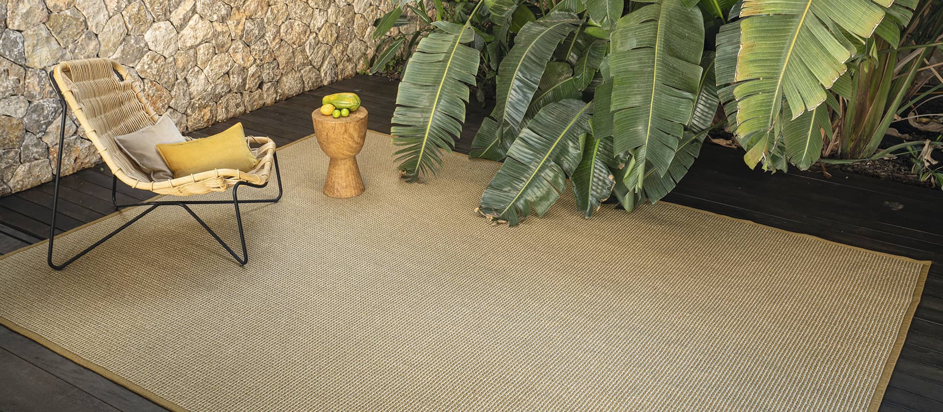Outdoor-Lounge mit einem Rattan-Sessel und Teppich in beige