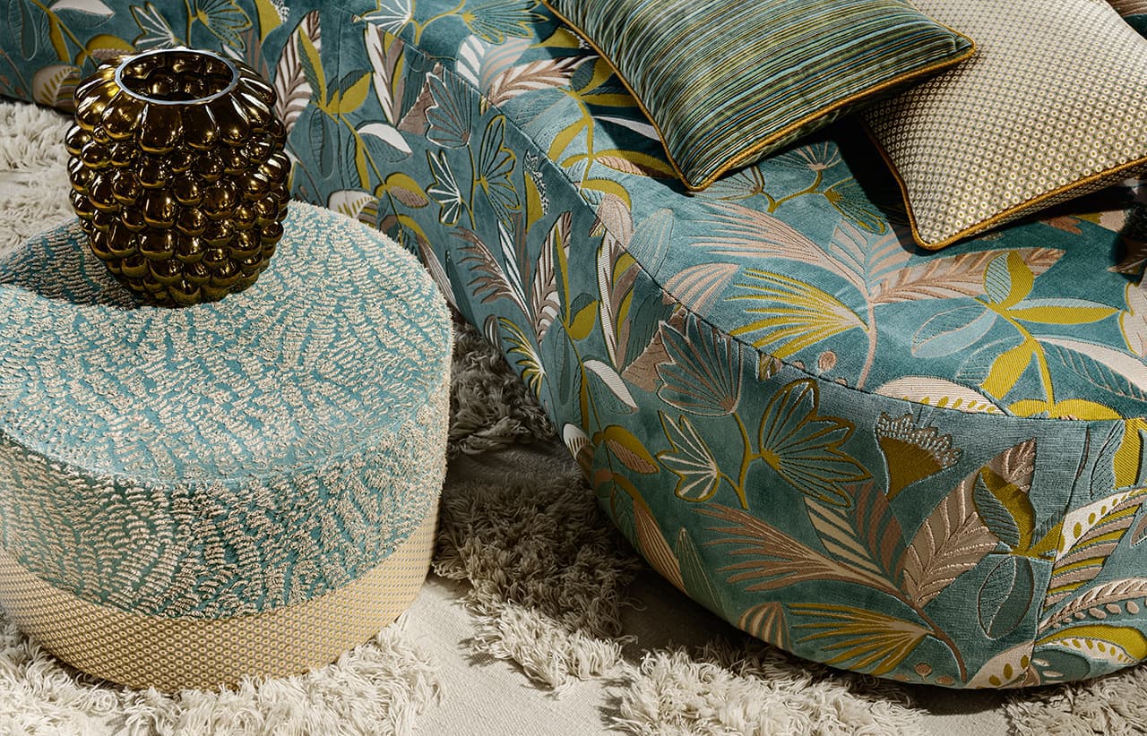 Ein Sofa mit floralem Muster und ein Pouf in grün und gold.