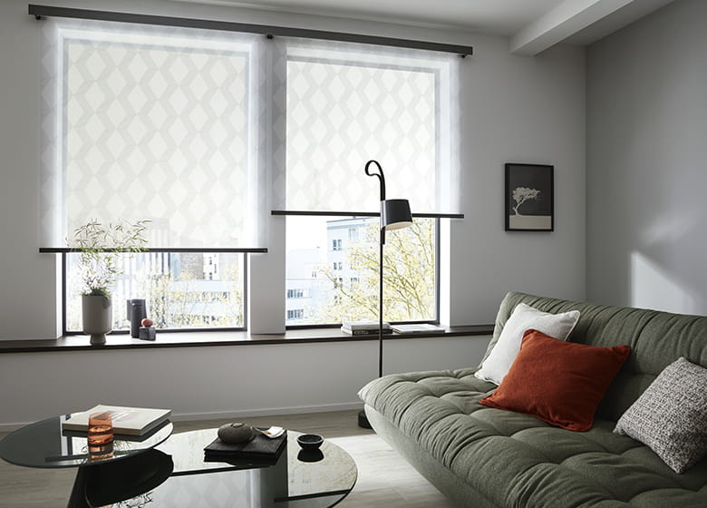 Sofa in gedecktem grün neben einer schwarzen Stehlampe und weiße Rollos mit Rautenmuster am Fenster