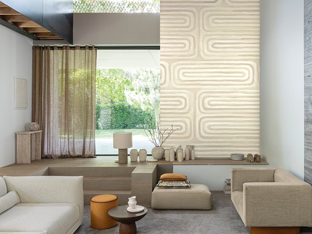 Das Bild zeigt ein Wohnzimmer mit Möbeln in Creme und Beige. Ein Fenster, das drei Stufen höher auf Podesthöhe angebracht ist, bringt viel Licht in den Raum. Die farblich abgestimmten Elemente schaffen eine helle und wohnliche Atmosphäre.