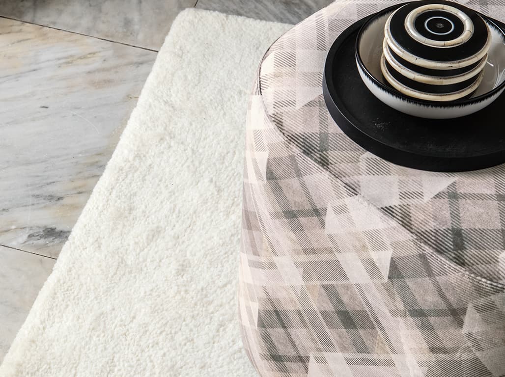 Das Bild zeigt einen weißen Teppich unter einem rosafarbenen, bemusterten Pouf. Die schwarz-weiße Dekoration sorgt für Abwechslung und ergänzt das Gesamtbild.