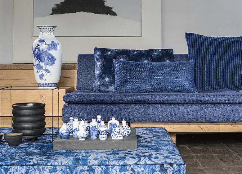 Das Bild zeigt ein Wohnzimmer mit einem blauen Sofa, Kissen und Tisch. Die überwiegende blaue Farbgebung schafft eine harmonische Atmosphäre.