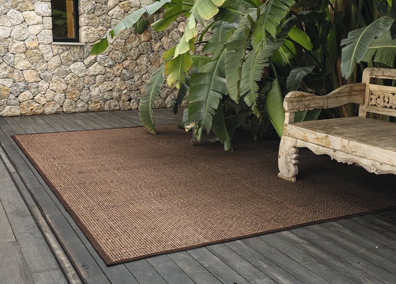 Outdoor-Lounge mit einer Sitzbank aus Holz, einer Steinwand und einem Teppich in braun