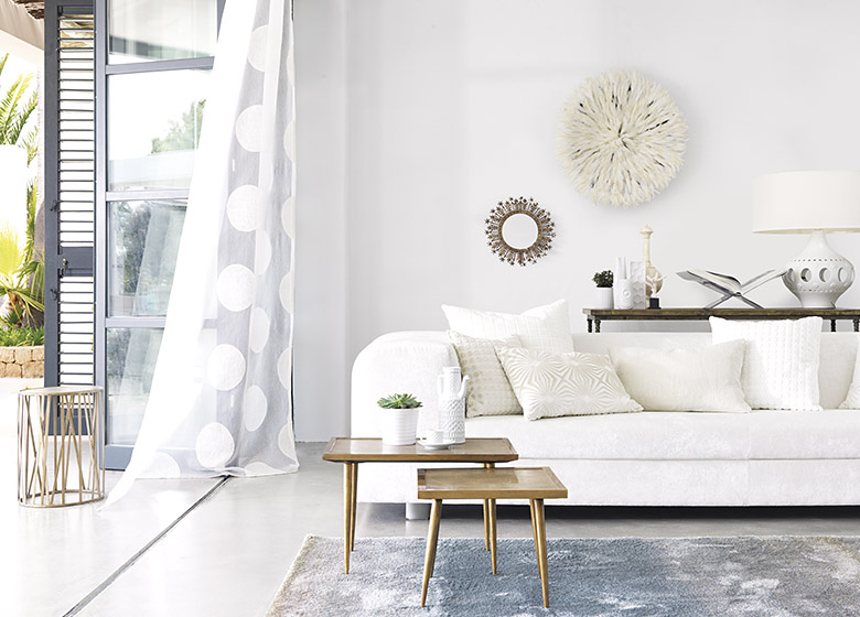 Das Bild zeigt einen überwiegend hell gestalteten Raum mit einem weißen Sofa. Verschiedene Accessoires sorgen für farbliche Abwechslung in dem vorwiegend weißen Ambiente.